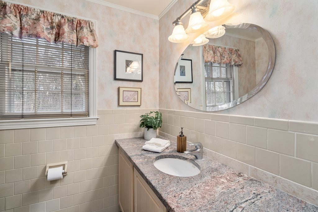 Bathroom vanity with a granite countertop, oval mirror, and window with floral curtains.