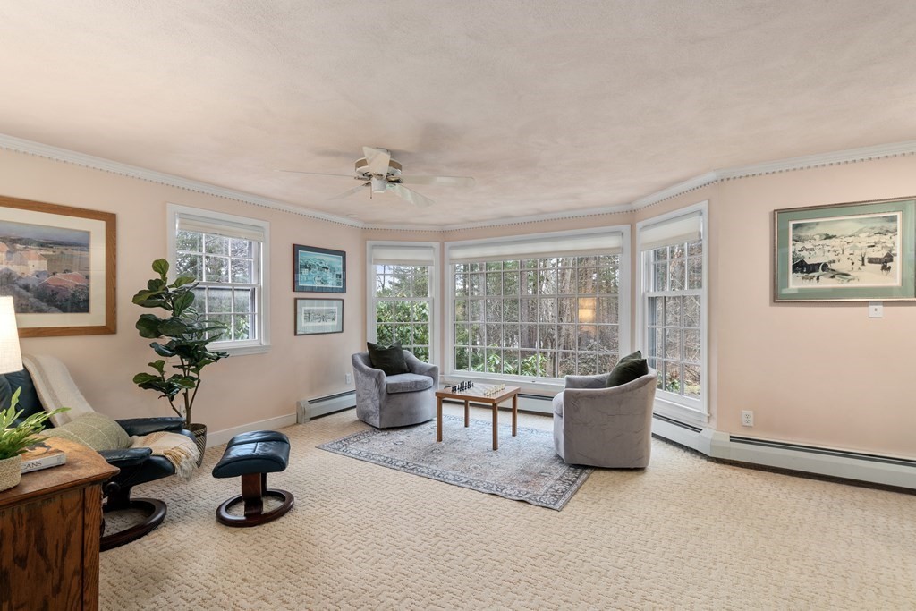 Living room with gray armchairs, cream carpet, and a large bay window overlooking trees.