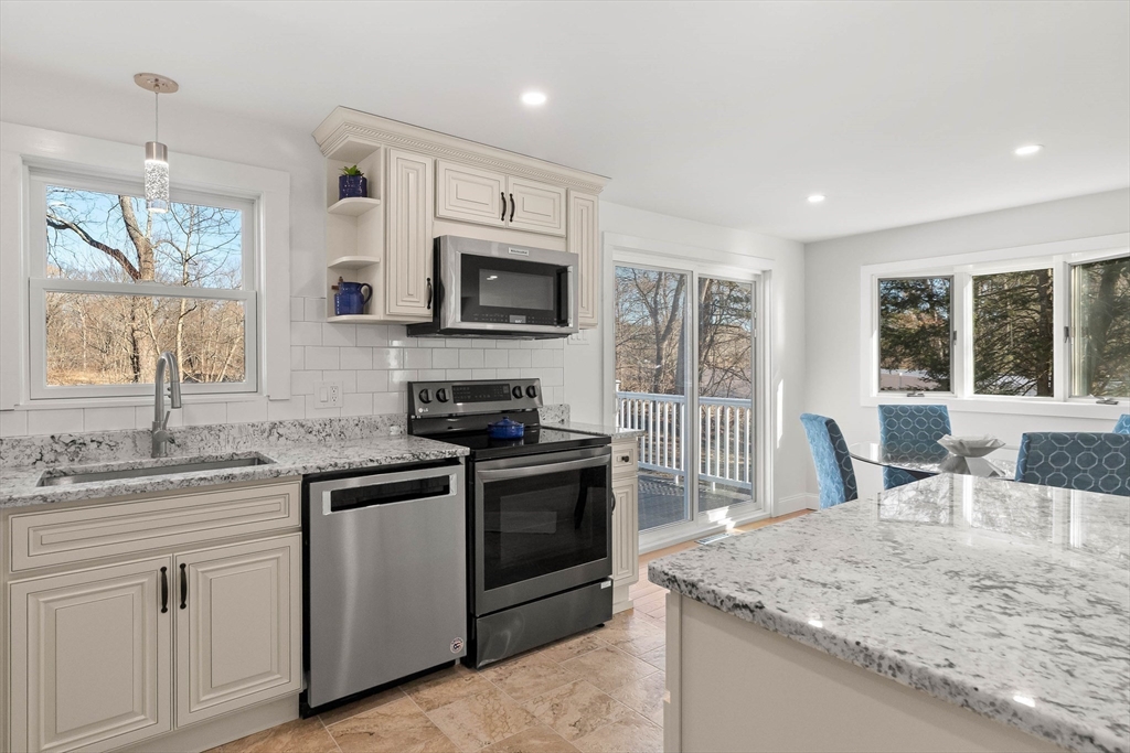 Kitchen with granite counters, white cabinetry, stainless appliances, and sliding doors to a tree-lined deck.