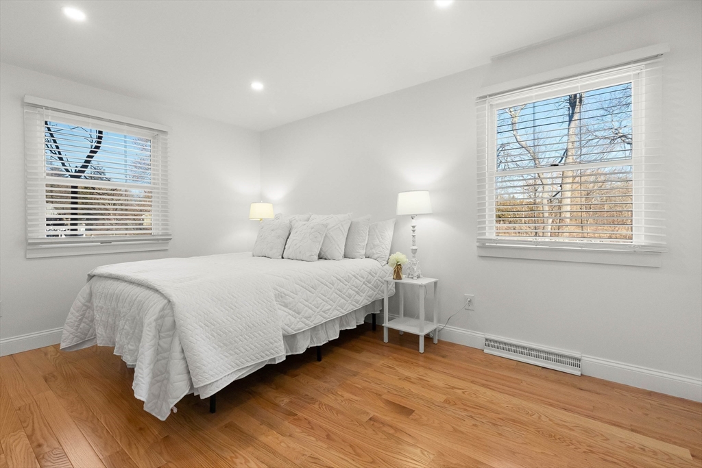 Bright bedroom with a white quilted bed, two windows, and warm hardwood floors.