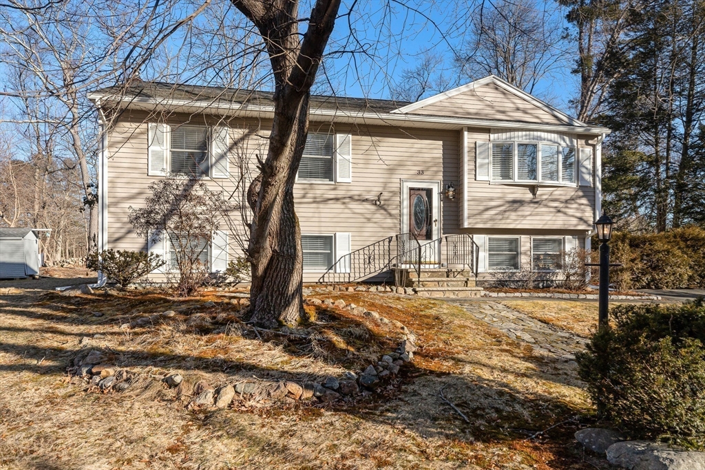 Beige split-level house with a large leafless tree and stone garden border in front.
