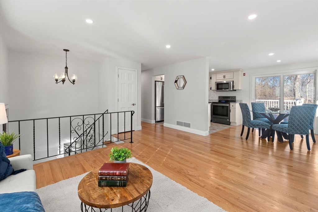 Open-plan living and dining area with hardwood floors, black stair railing, and kitchen beyond.