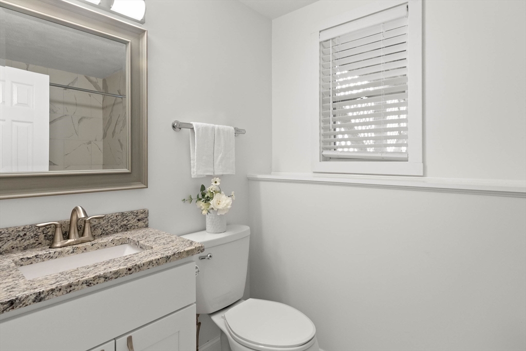 Bathroom with a granite vanity, toilet, and window with white blinds.