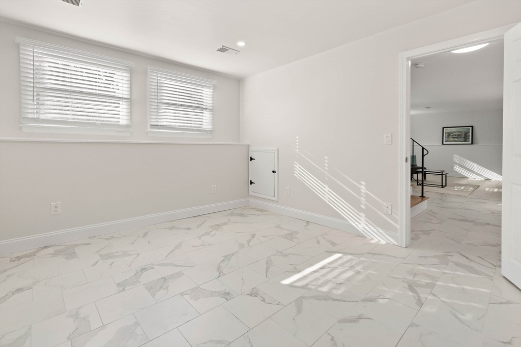 Empty room with marble-look tile floors, two windows with blinds, and a doorway to a sitting area.