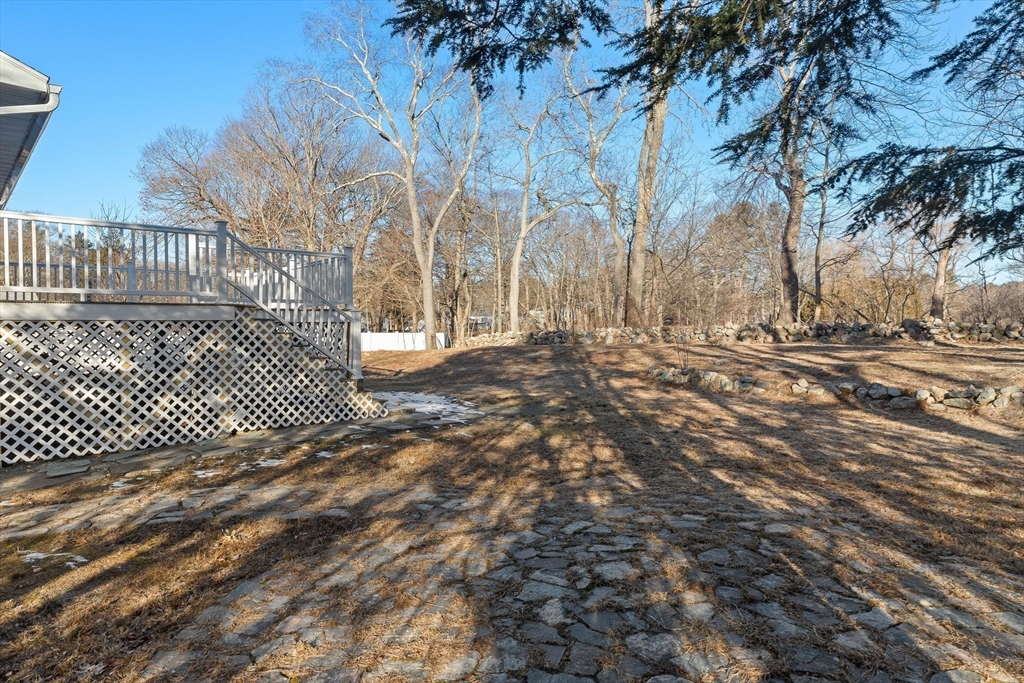 Backyard with a raised deck, stone path, and leafless trees along the wooded edge.