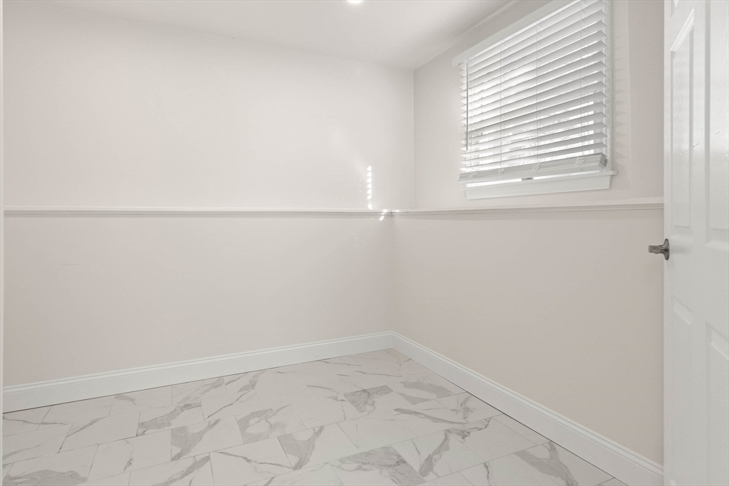 Empty room with marble-pattern tile flooring and a window with white blinds.