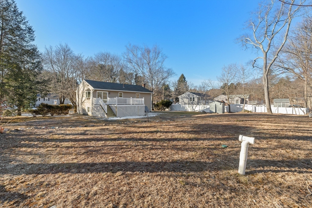 Back of a beige house with a raised deck beyond a wide dormant yard and white fencing.