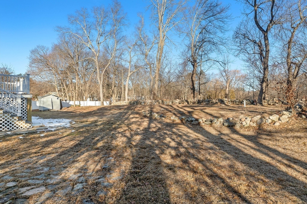 Backyard with a stone retaining wall, raised deck, and small shed among leafless trees.