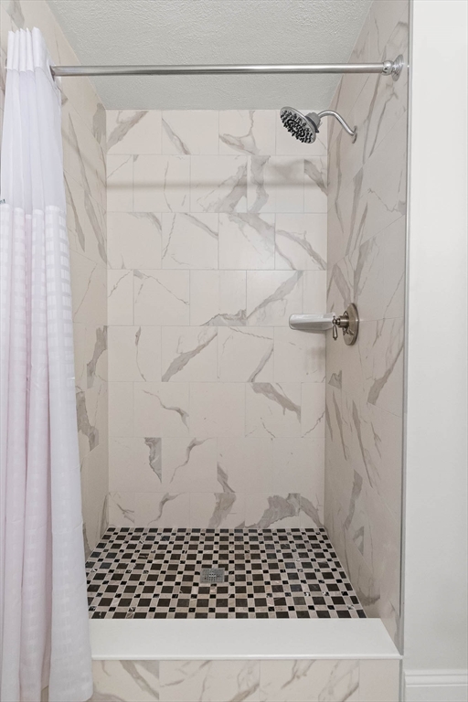 Walk-in shower with marble-look tile, checkerboard floor, and chrome fixtures.