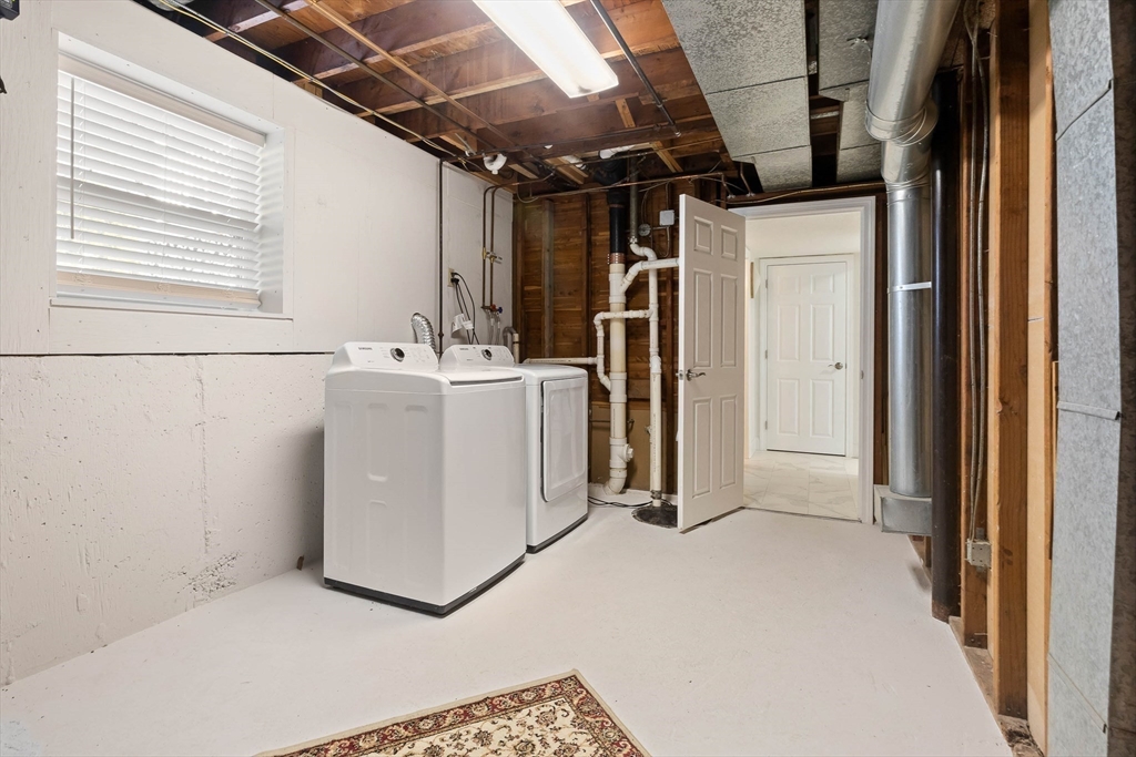 Basement laundry area with a washer and dryer beneath exposed ceiling joists.