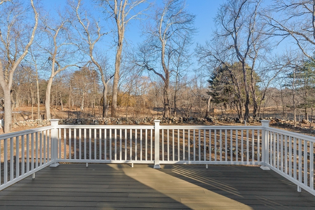 Composite deck with white railings overlooking a leafless wooded yard and stone wall.