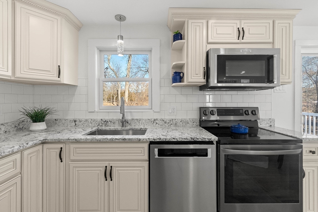 Kitchen with cream cabinets, granite counters, stainless appliances, and a window overlooking trees.