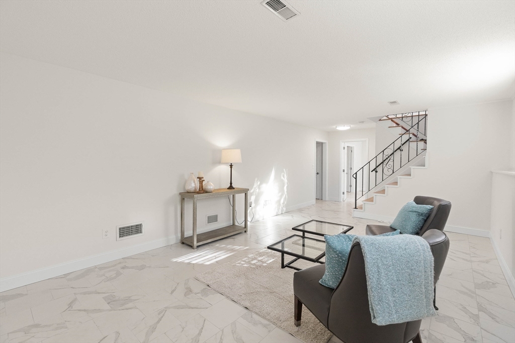 Furnished living room with marble-look tile floors, blue throws, and a staircase with black railing.