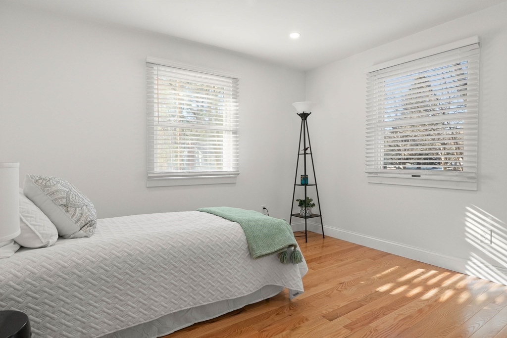 Bedroom with a white quilted bed, mint throw, and two sunlit windows above hardwood floors.