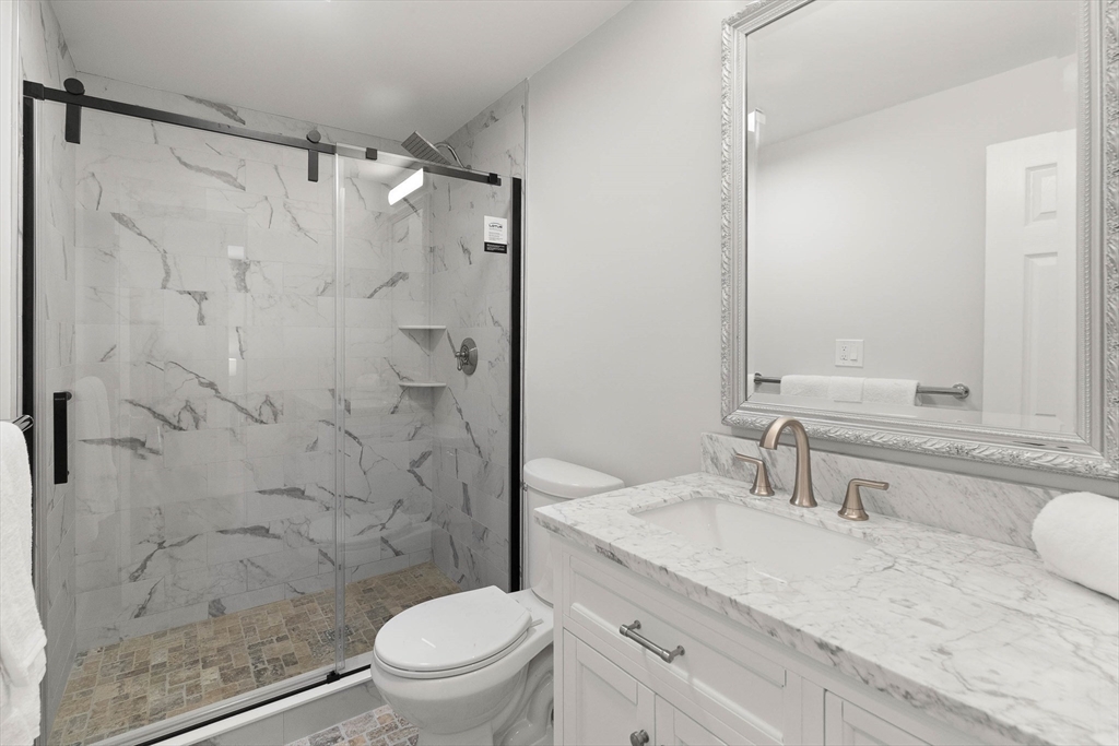 Bathroom with a marble-look walk-in shower, mosaic floor, and white vanity with bronze fixtures.