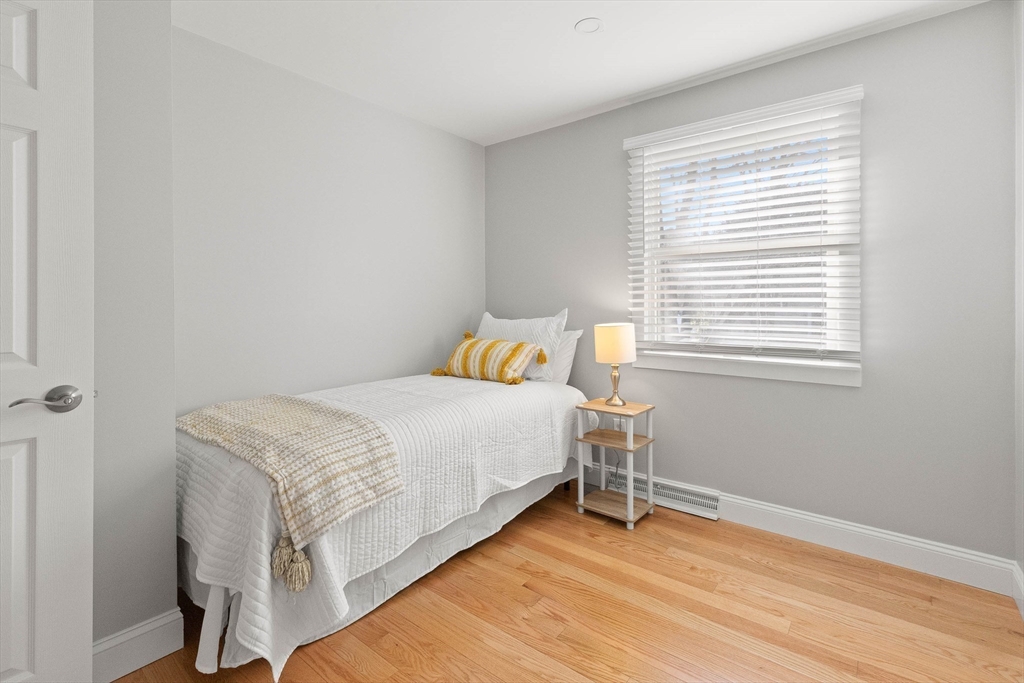 Staged bedroom with a white bed, yellow-striped accents, bedside lamp, and wood flooring.