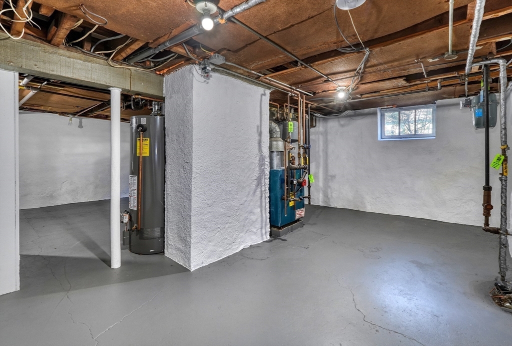 Unfinished basement utility area with exposed pipes, a water heater, and a small window.