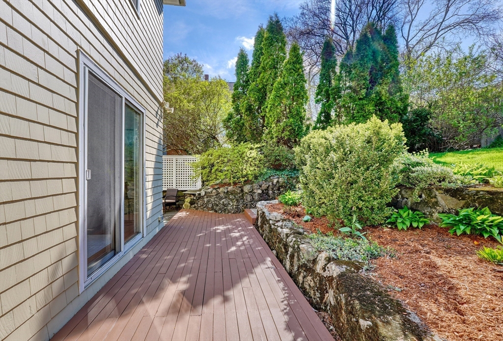 Wood deck beside the home, bordered by a stone retaining wall and landscaped garden.