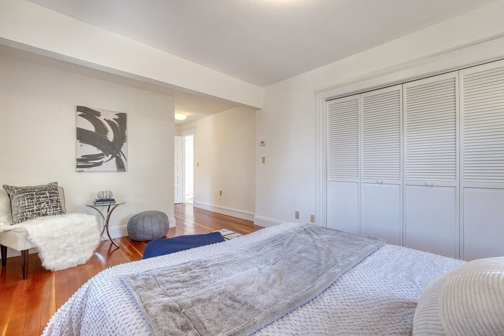 Bedroom with hardwood floors, white louvered closets, and a small sitting area.