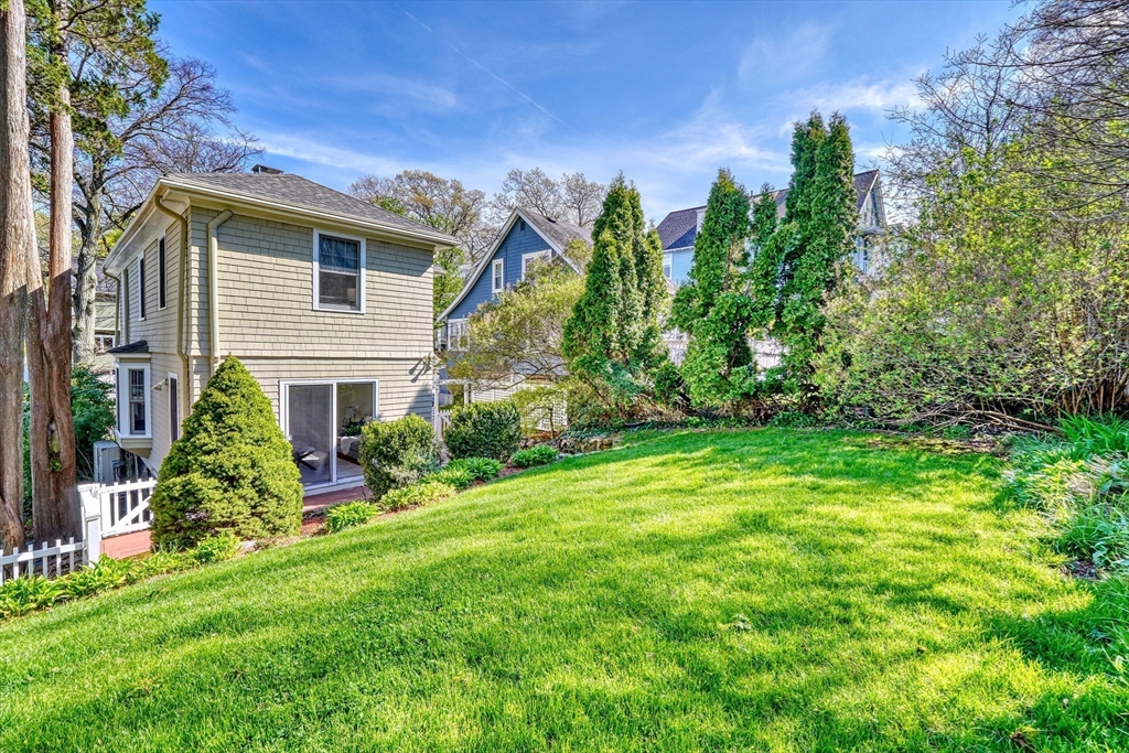 Home’s backyard with a broad lawn, mature trees, and landscaped shrubs.