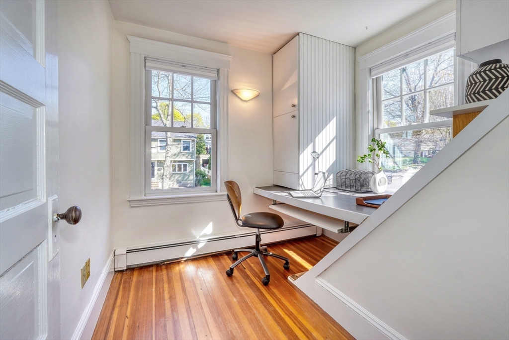 Home office with a built-in desk between two sunny windows and polished hardwood floors.