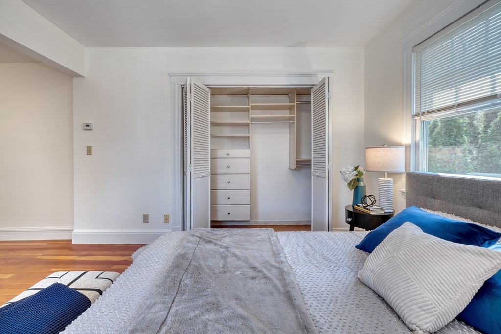 Bedroom with an open built-in closet, white and blue bedding, and a window with blinds.