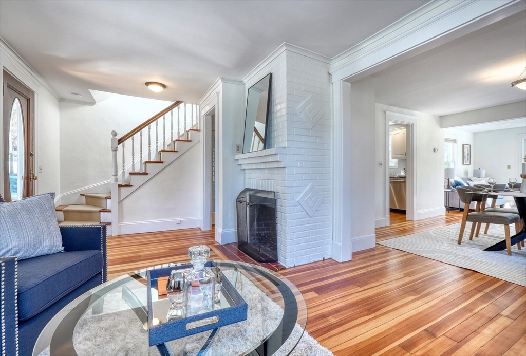 Living room with a white brick fireplace, hardwood floors, and a staircase beside the adjoining dining area.