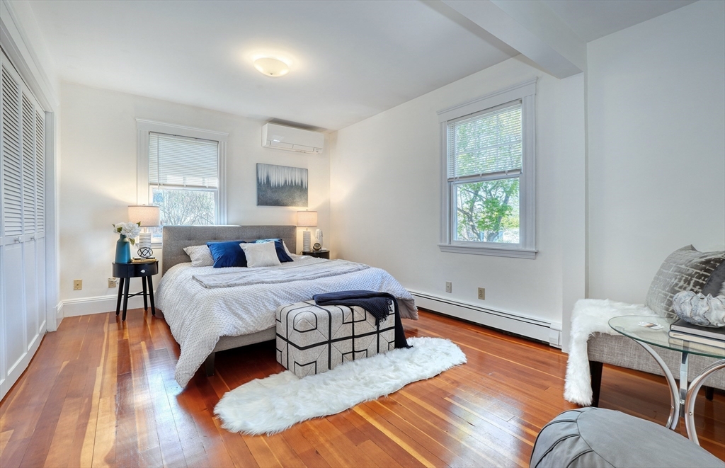 Bright staged bedroom with hardwood floors, two windows, and a king bed.