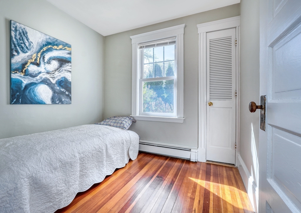 Bedroom with a white-quilted bed, abstract blue wall art, and polished hardwood floors.
