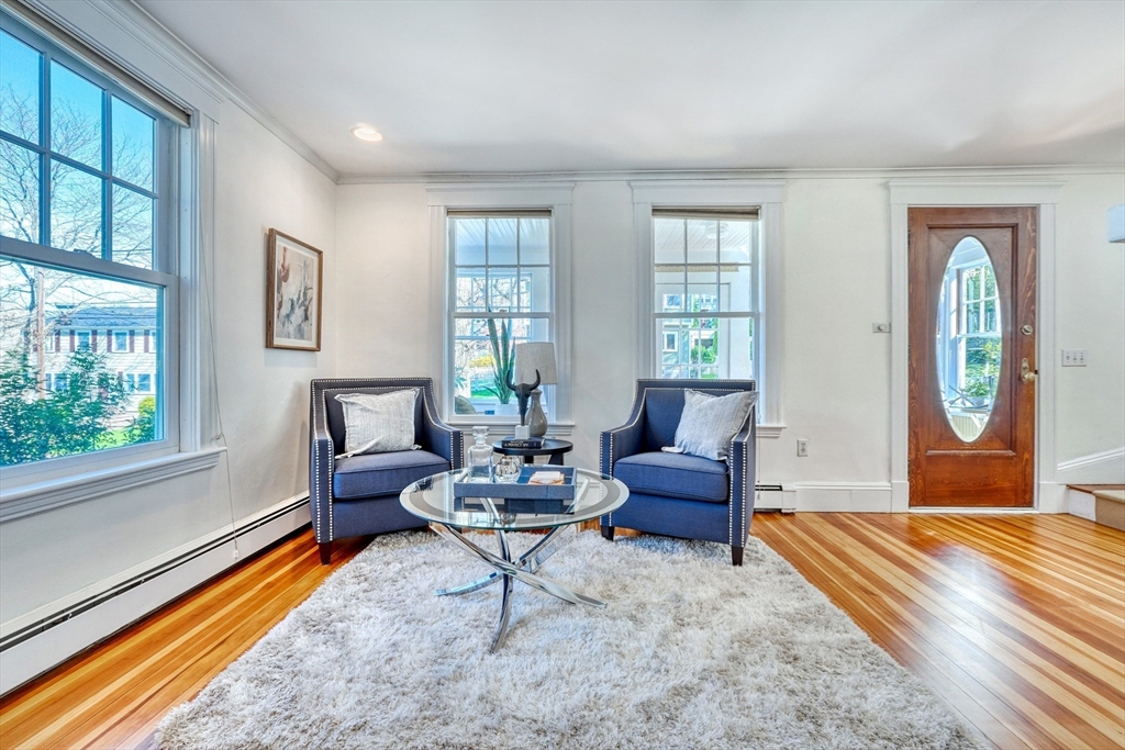 Living room with blue armchairs, a glass coffee table, tall windows, and polished hardwood floors.