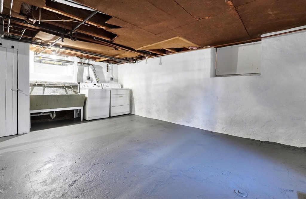Basement laundry area with a utility sink, washer, dryer, and exposed ceiling joists.