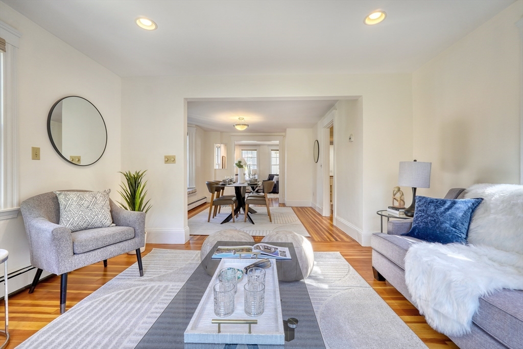 Staged living room with gray seating and hardwood floors, opening to a dining room.