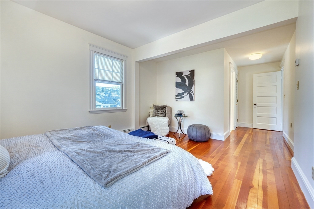 Staged bedroom with hardwood floors, a large bed, and a cozy sitting nook.
