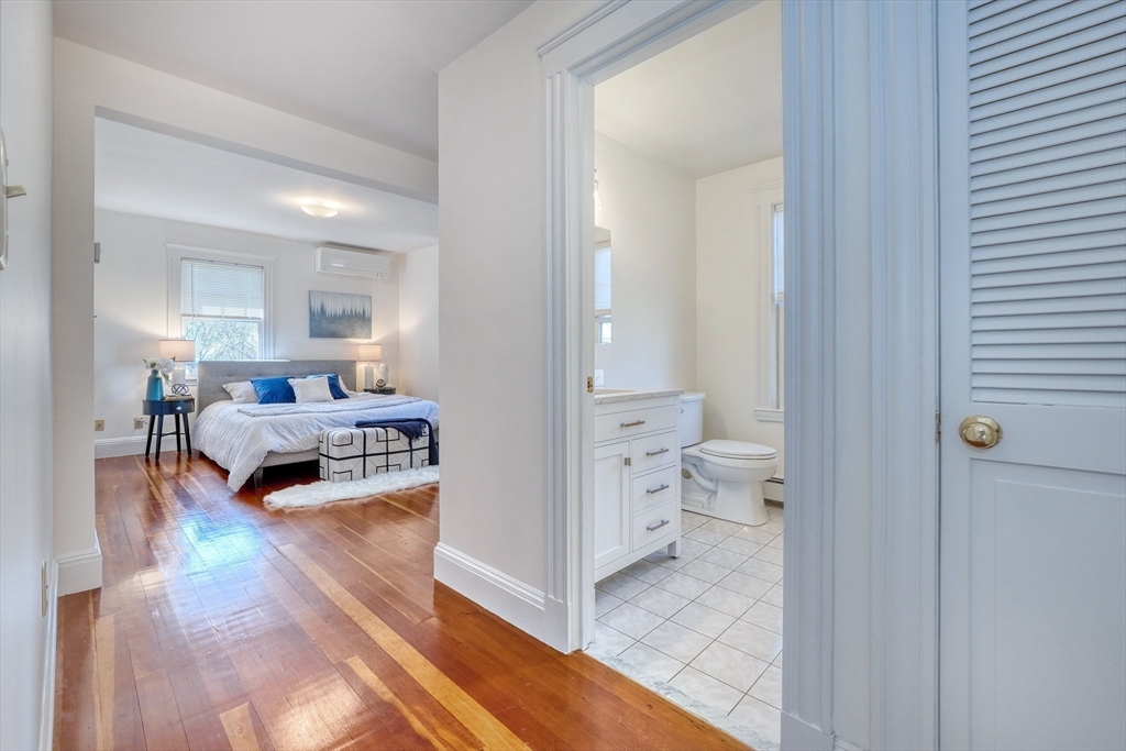 Furnished bedroom with hardwood floors and an adjoining bathroom visible through the open doorway.