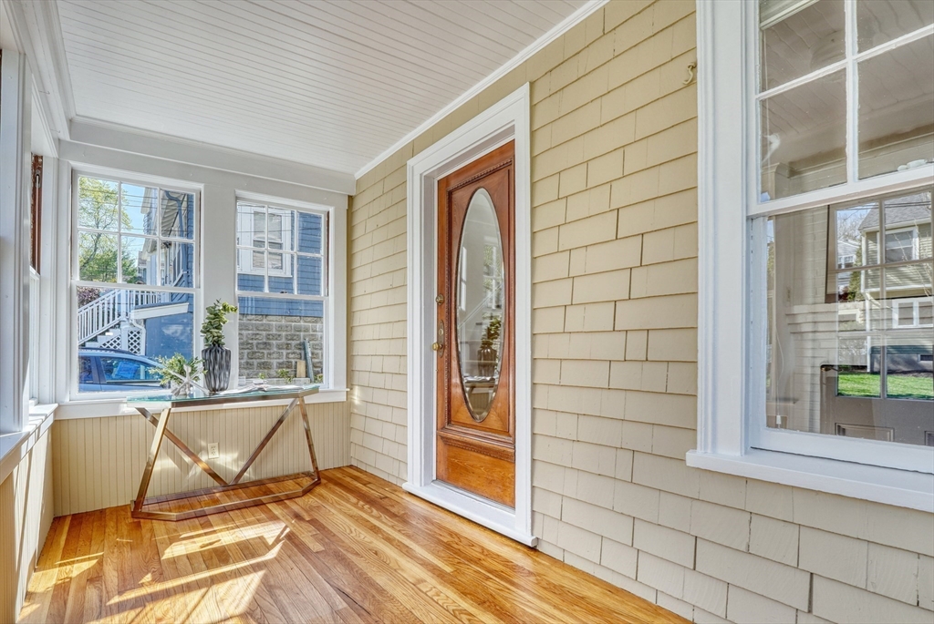 Enclosed porch with hardwood floors, large windows, and a wood entry door.