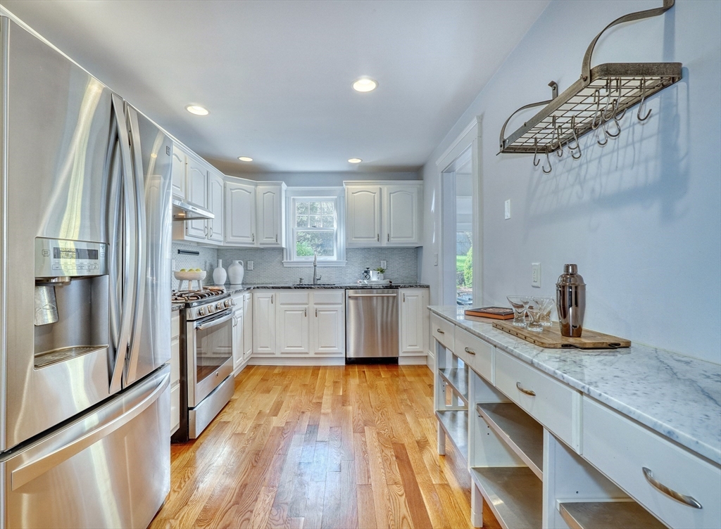 Renovated kitchen with white cabinets, stainless steel appliances, marble counters, and warm wood floors.