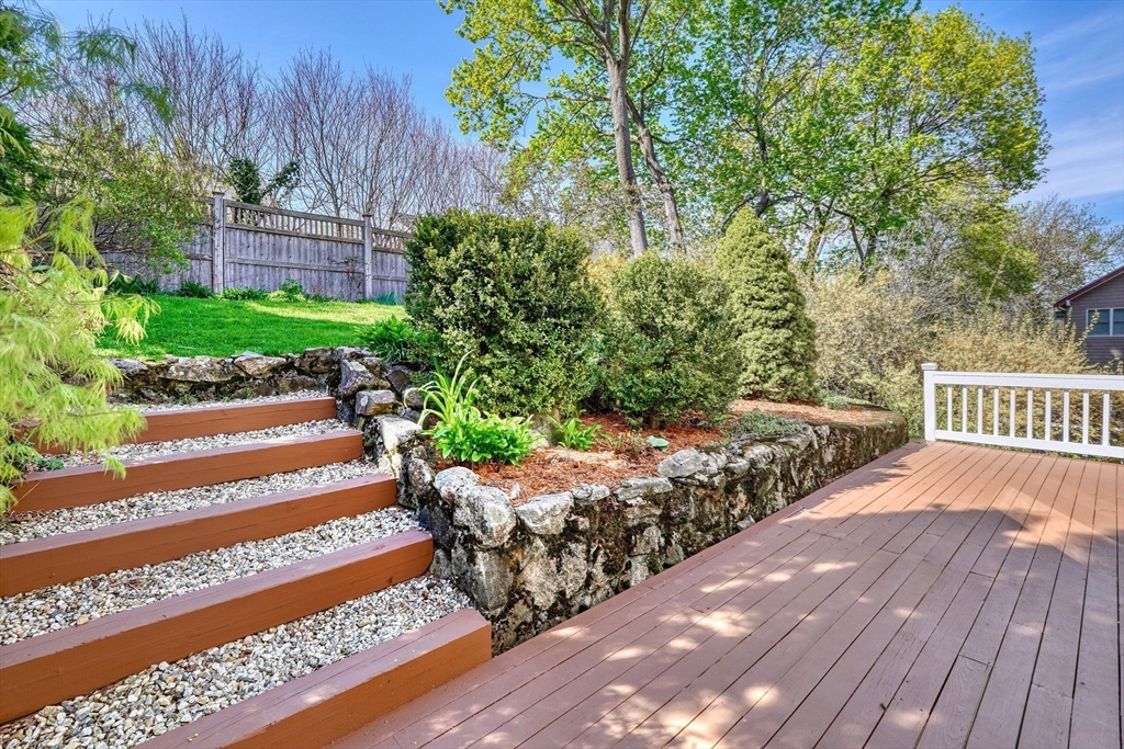 Backyard deck with white railing, gravel steps, stone retaining wall, and landscaped slope.
