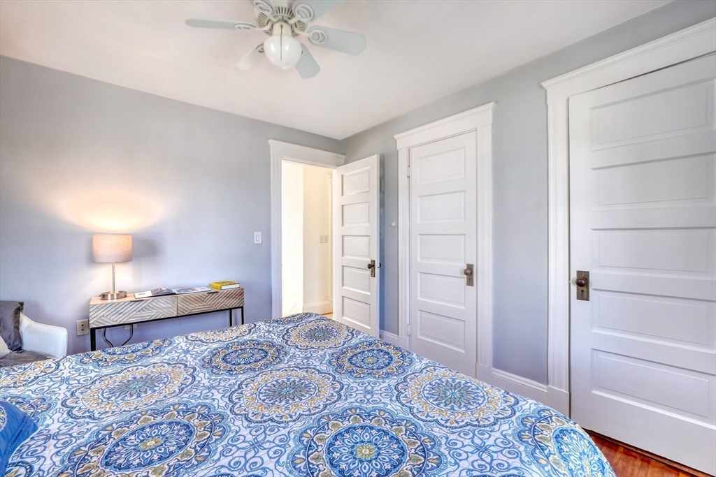 Bedroom with a blue patterned bedspread, pale gray walls, and white paneled doors.