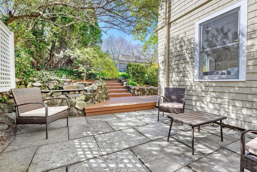 Stone patio beside the house with wicker seating and steps leading into a landscaped garden.