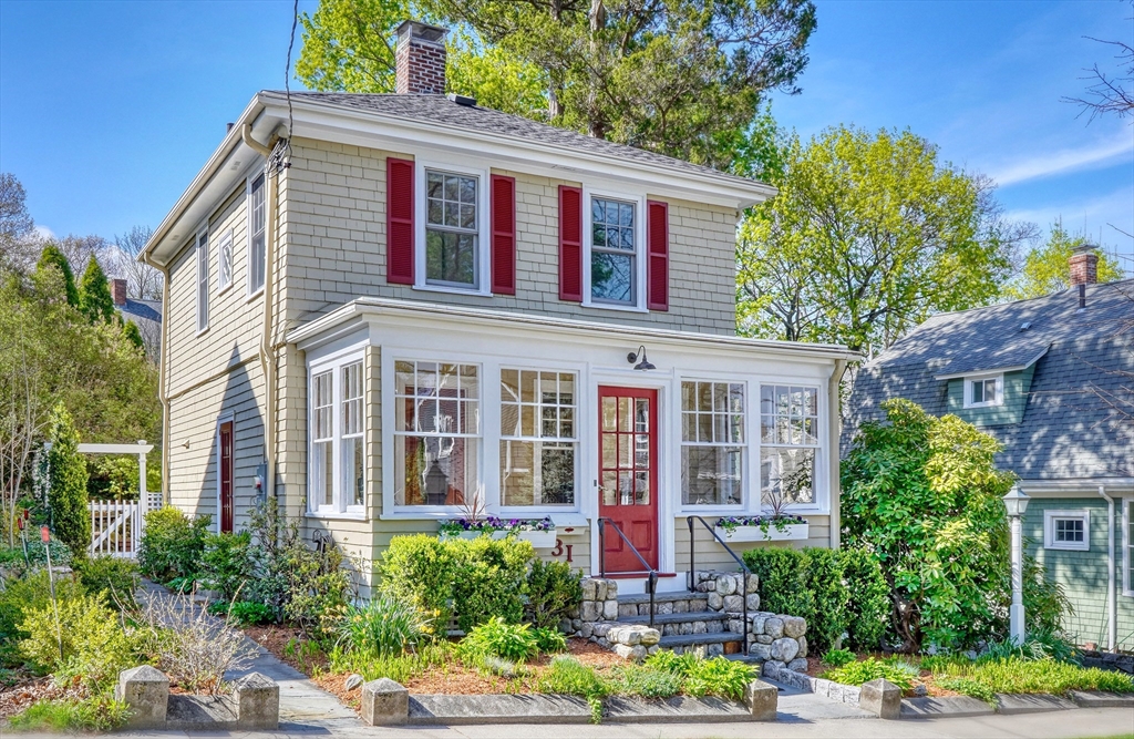 Two-story shingle house with red shutters and entry door, stone steps, and landscaped front garden.