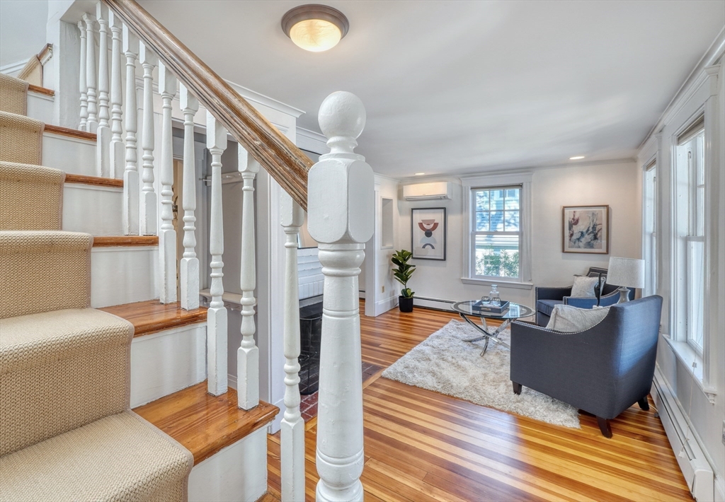 Living room with a prominent staircase, polished hardwood floors, fireplace, and blue armchairs.