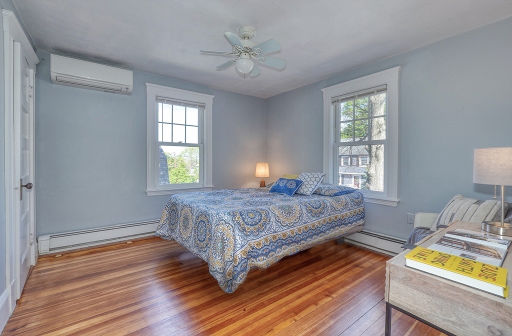 Bedroom with a patterned blue bedspread, two windows, and polished hardwood floors.