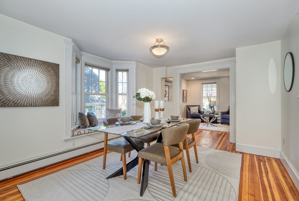 Dining room with a glass-top table beside bay windows and an adjoining sitting room.