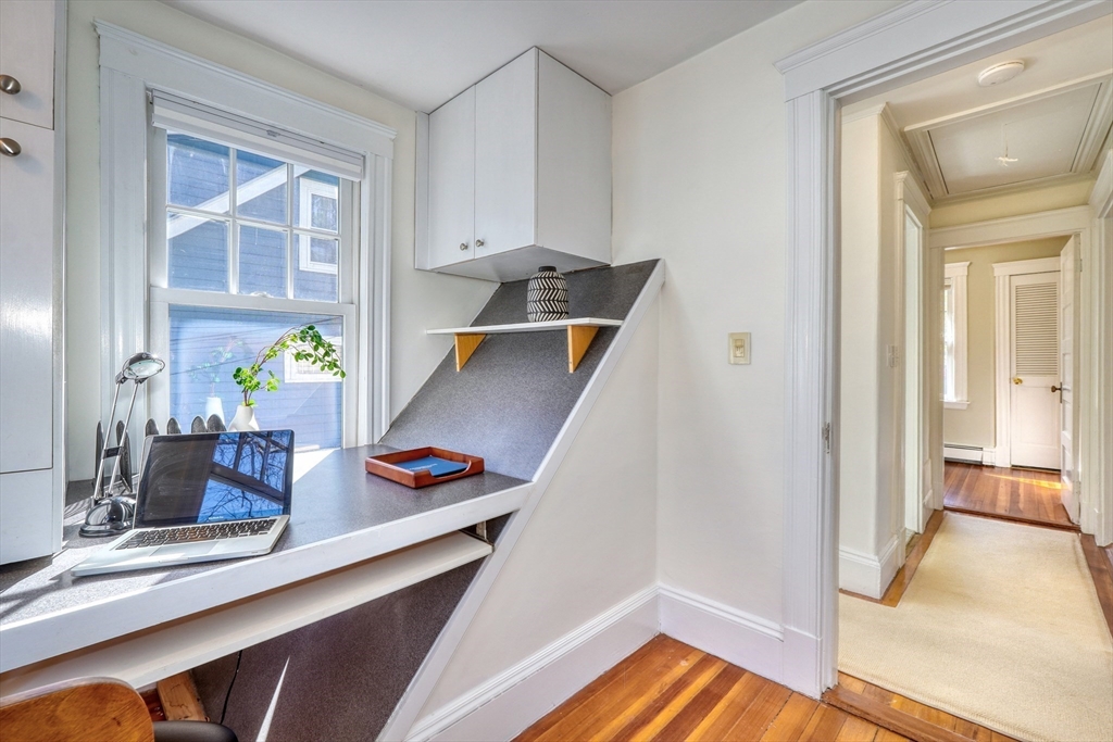 Built-in home office desk beneath a window, with a laptop and hallway beyond.