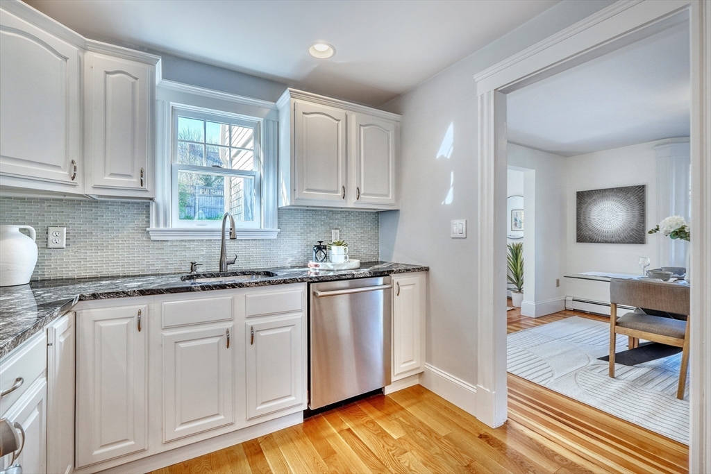 Kitchen with white cabinets, gray tile backsplash, granite counters, and stainless steel dishwasher.
