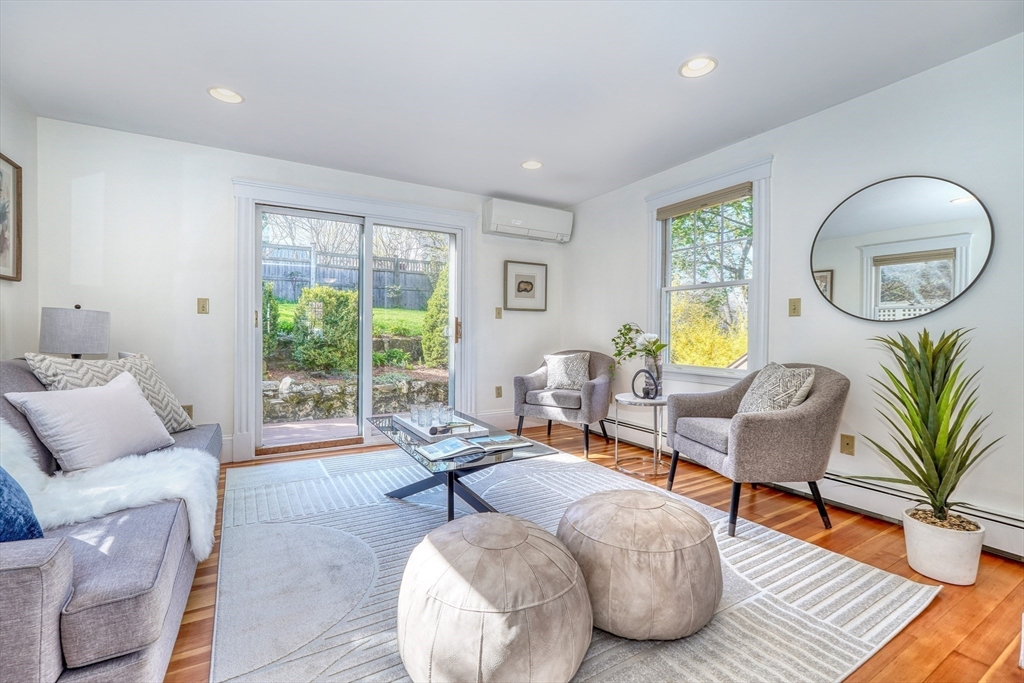 Living room with hardwood floors, gray seating, round ottomans, and sliding doors to a garden.