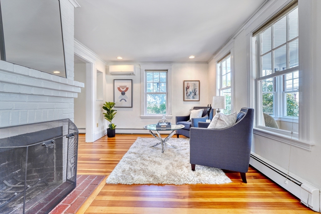 Living room with a white brick fireplace, blue armchairs, tall windows, and polished hardwood floors.