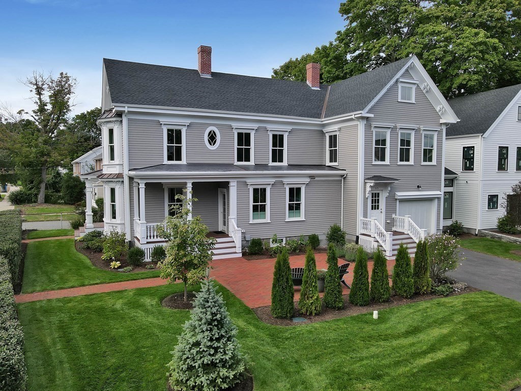 Gray two-story house with a covered porch, brick patio, and landscaped lawn.