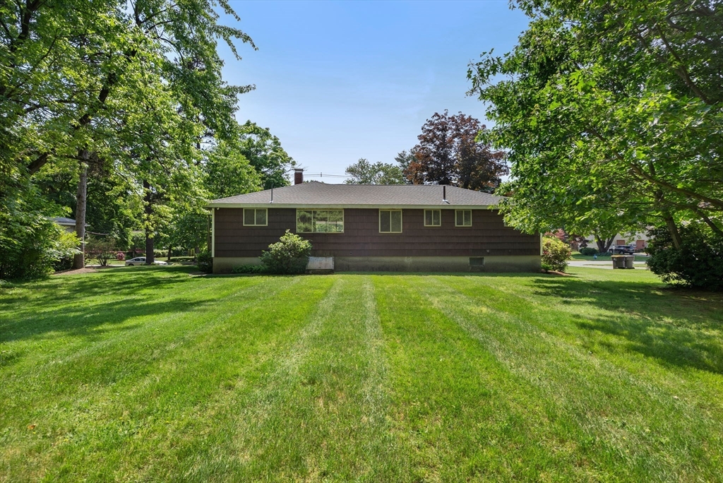 Single-story brown home beyond a broad lawn, framed by mature leafy trees.