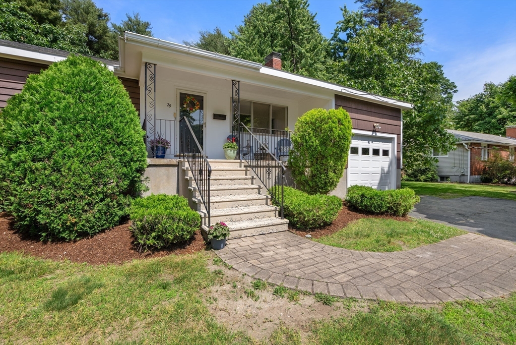 Single-story home with a covered entrance, concrete steps, black railings, and landscaped shrubs.